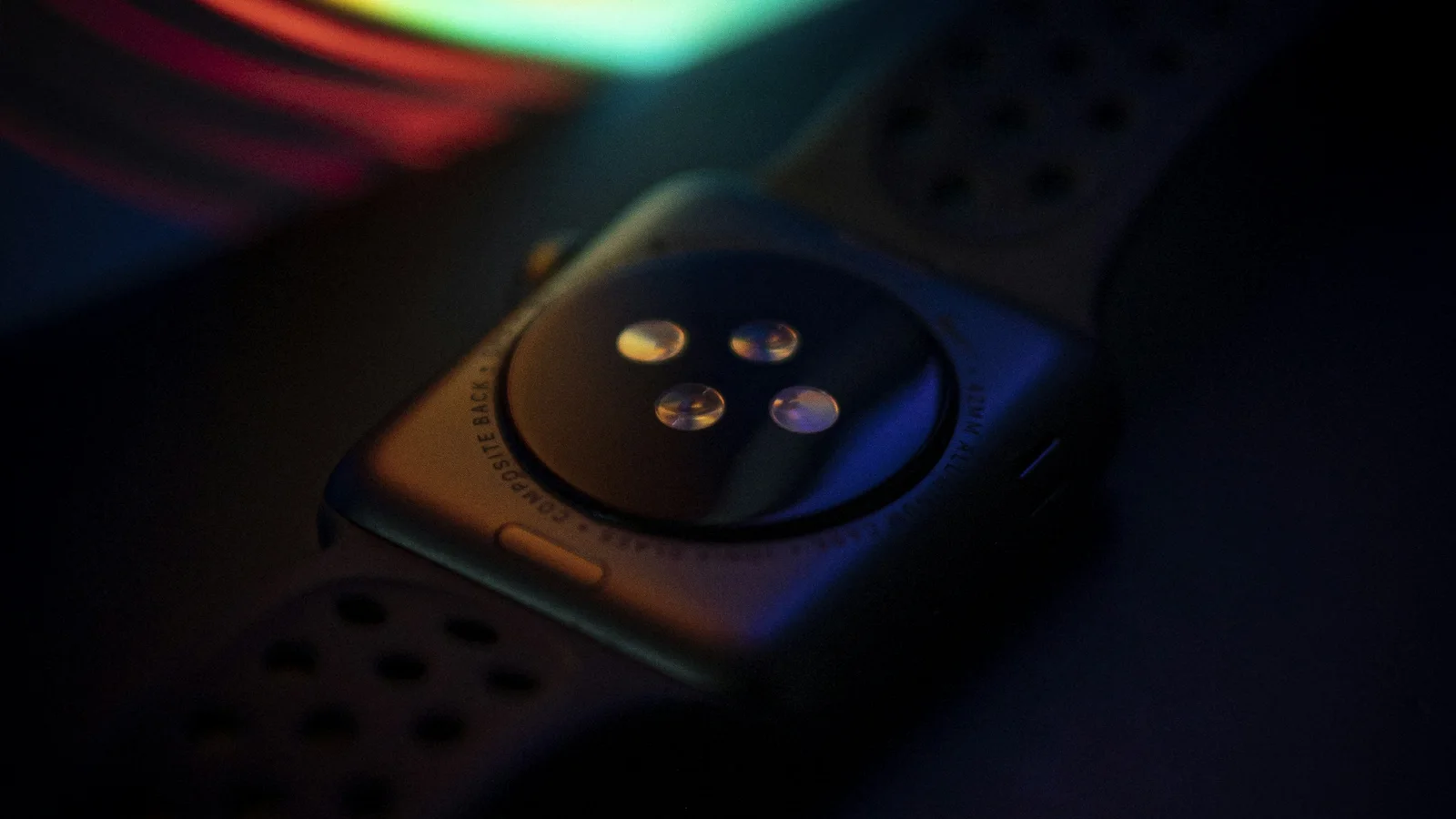 Back of an Apple Watch optical heart sensor under colored light